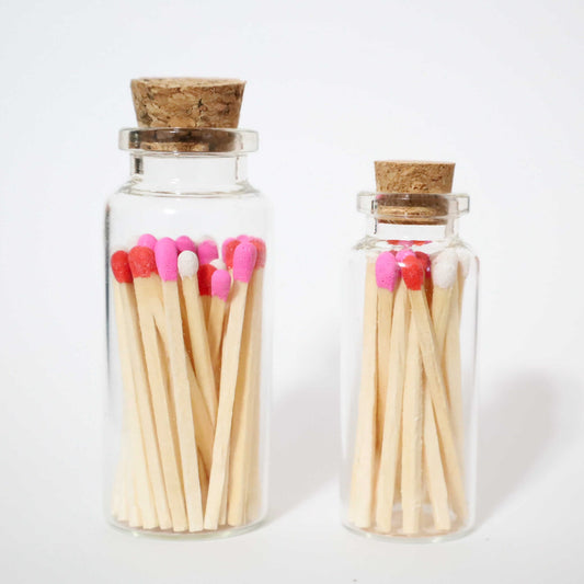 1 small glass bottle and 1 bigger glass bottle with cork cap with hot pink, red and white safety matches inside